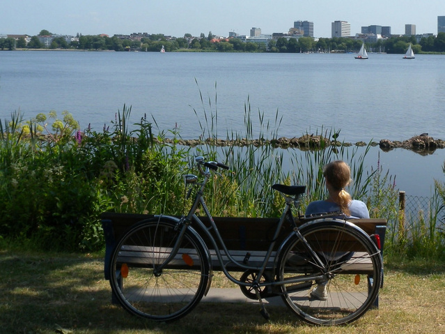 Photo of a person sitting on a bench with a lake in the background
